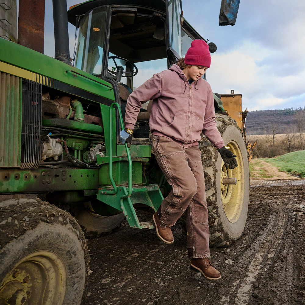 A woman climbing out of a tractor wearing the Elm 8" Waterproof Logger in brown.
